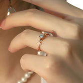 Hand wearing rose-gold vine solitaire diamond ring with pearl necklace in background